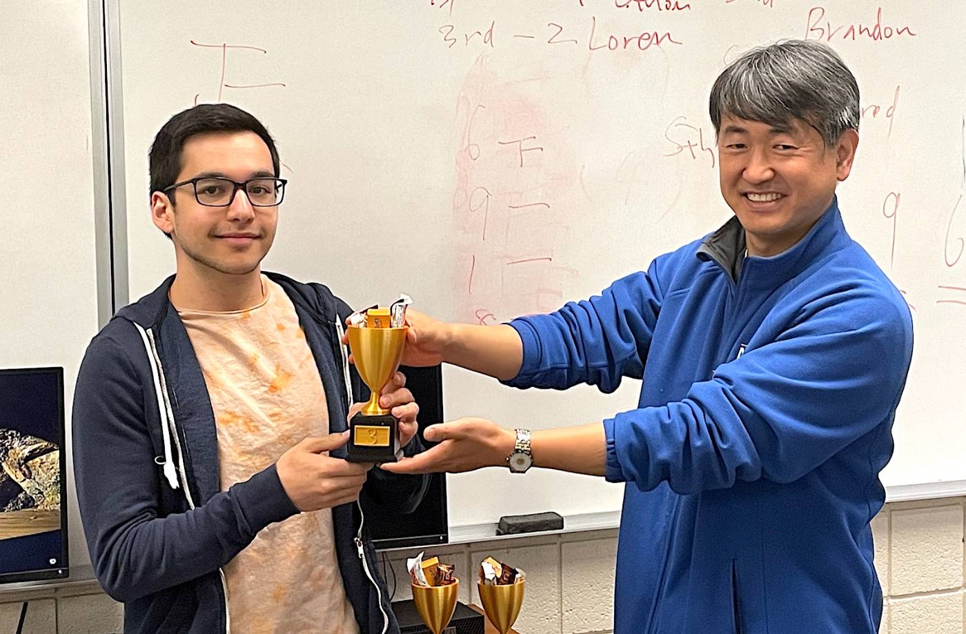 IT student and instructor in classroom with competition trophy